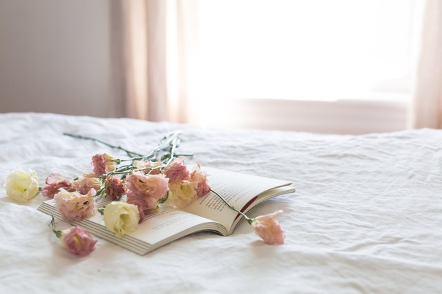rozevřená kniha a květiny na posteli